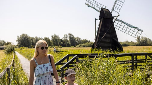 A lady and a boy walk along the boardwalk at Wicken Fen, beside the windpump